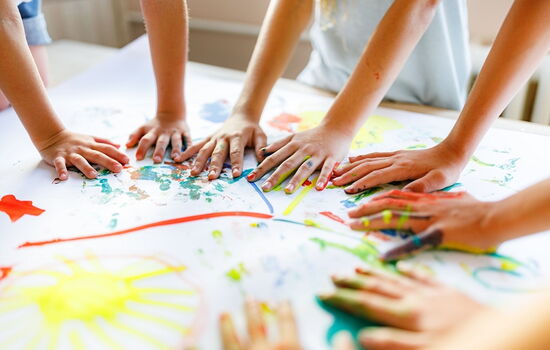 Man sieht nur die Hände von Kindern, die mit Fingerfarben ein buntes Bild malen