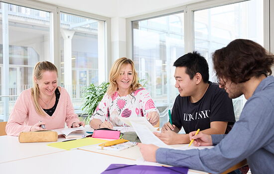 Männer und Frauen unterschiedlichen Alters und mit unterschiedlicher Herkunft sitzen an einem Tisch und lernen miteinander.