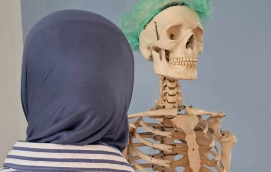 Man sieht eine Frau mit Hijab von hinten, die auf ein Skelett blickt