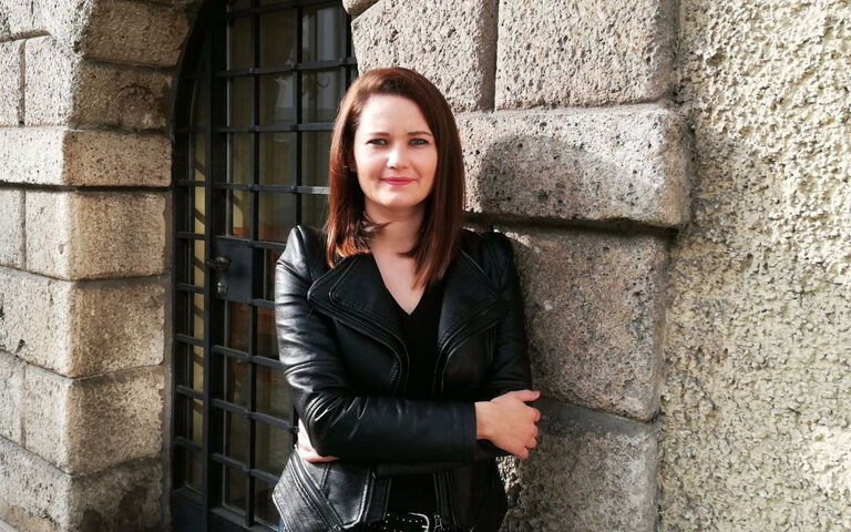 Das ist ein Bild, auf dem Brigitta Lajko an einer Hausmauer lehnt