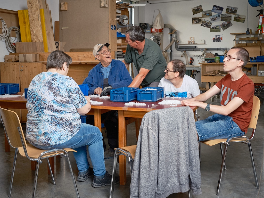 Menschen sitzen an einem Tisch und verrichten gemeinsam eine Arbeit